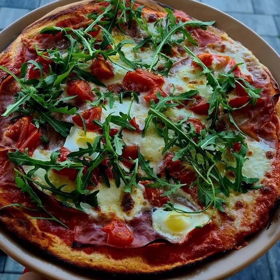 Pizza s rukolou, rajčaty, šunkou a volským okem na talíři
